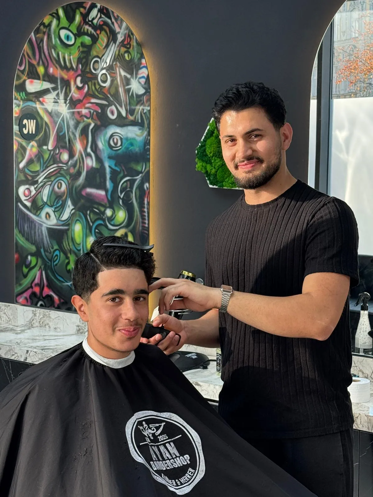 Barbier stylt die Haare eines Kunden vor dem Produktregal im Salon.